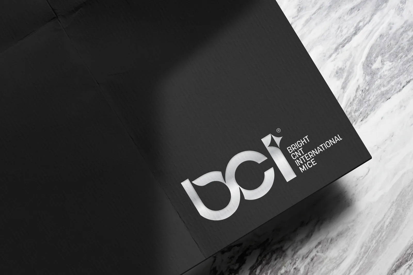 Siyah dokulu kâğıt üzerinde gümüş baskı BCI Bright CNT International MICE logosu, yanında mermer yüzey