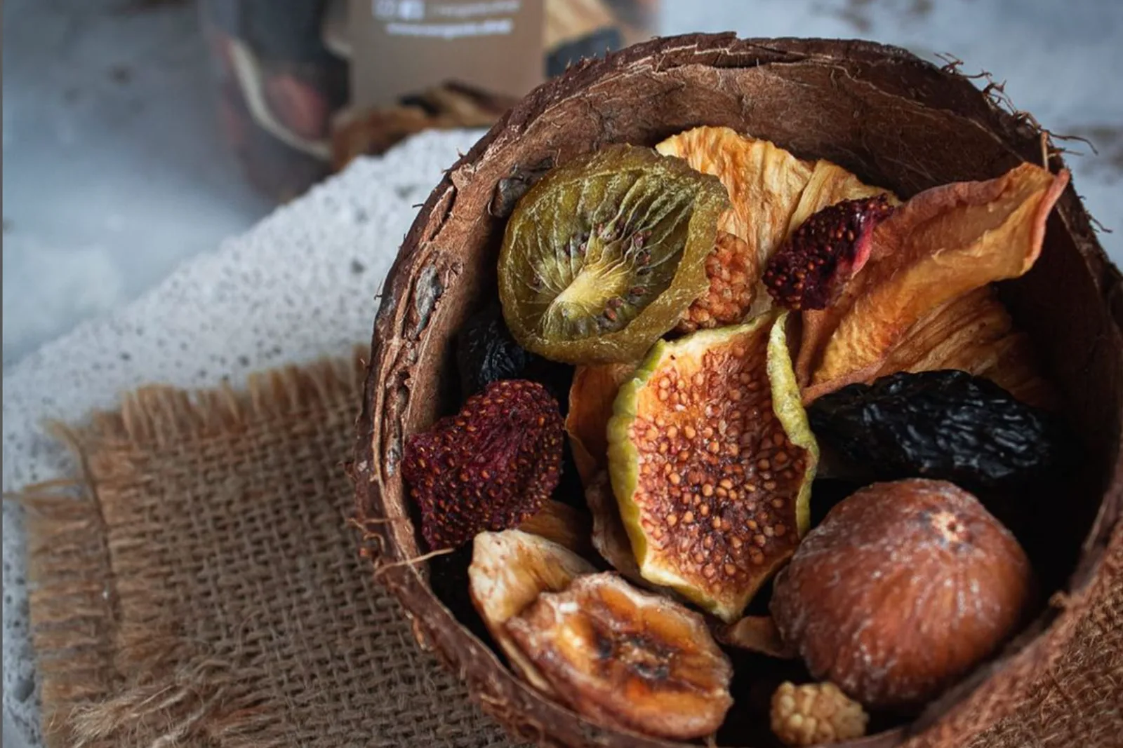 Hindistan cevizi kabuğundan bir kâsede kurutulmuş incir, kivi ve meyveler, çuval bezi üzerinde